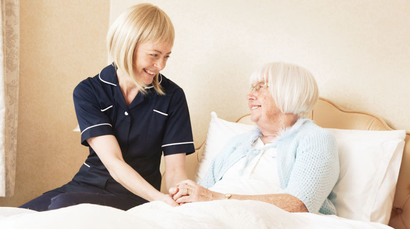 caregiver sitting on a bed with a senior woman who needs home care