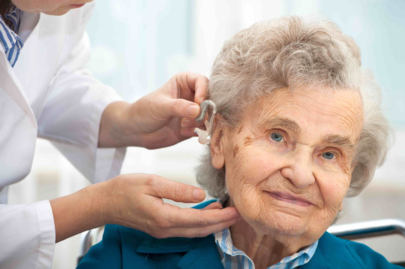 elderly women having hearing aid put on